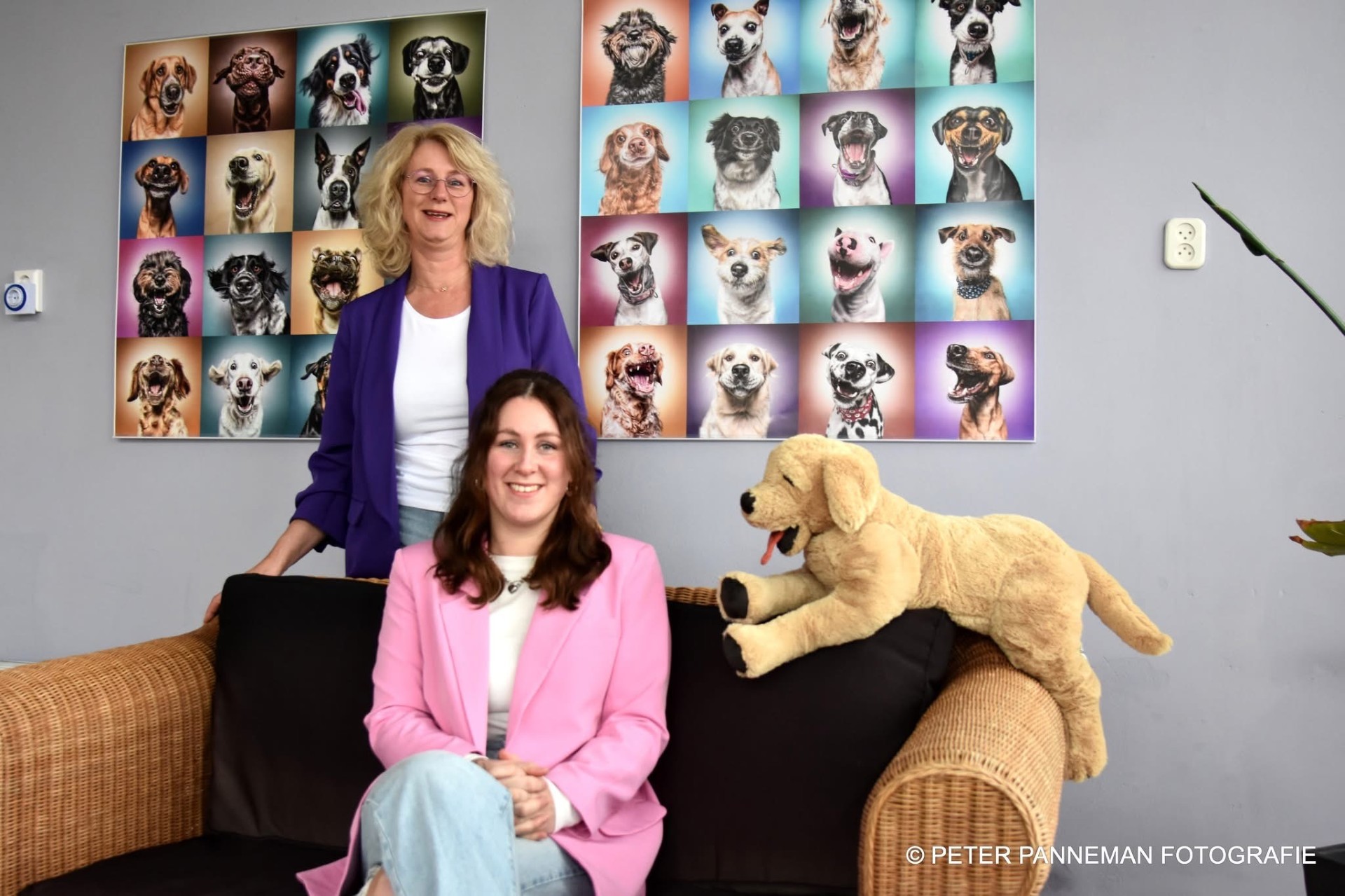 Esther en Romy op de bank in de salon, onder een wand vol kleurige hondenportretten